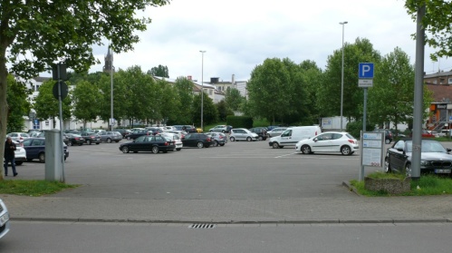 Asphaltierter, großer Parkplatz mit Markierungen. Parkende Fahrzeuge.