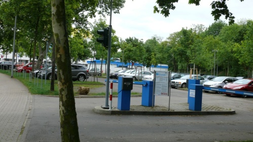 Ein- und Ausfahrt Parkplatz mit Schrankenanlagen, parkende Autos unter Bäumen