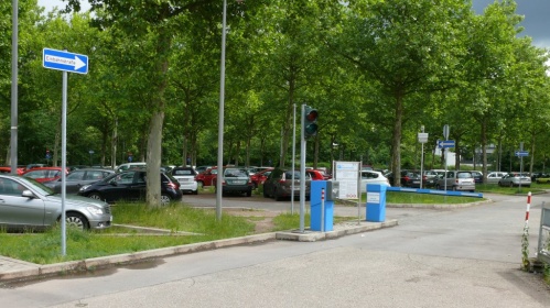 Zufahrt mit Schrankenanlage. Fahrzeuge stehen unter Bäumen.