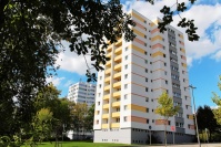 2 quadratische Hochhäuser mit 12 Etagen. Fassaden weiß. Farbakzente gelb/orange Haus vorne, hinten blau. Vorne hohe Bäume. 2 quadratische Hochhäuser mit 12 Etagen. Fassaden weiß. Farbakzente gelb/orange Haus vorne, hinten blau. Vorne hohe Bäume.