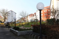 gepflasterter Fußweg, runde Laternen, Fahrradständer, eingefasstes und bepflanztes Beet, Grünflächen, Hecken.