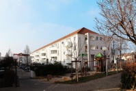 Gebäudezeile mit vier Wohnetagen in der Morgensonne. Fassade hell, vorne ein Spielplatz.