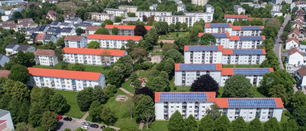 sanierte Wohnhäuser in weiß mit drei und vier Etagen. Gebäude rechts mit Solarpanels auf den Dächern.