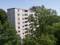 Hochhaus in Palttenbauweise. Fassade kleine Mosaikplatten. Rundum viele Bäume.