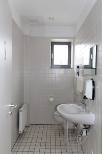 WC mit Handwaschbecken. Raum ist weiß gefliest und hat ein Fenster.