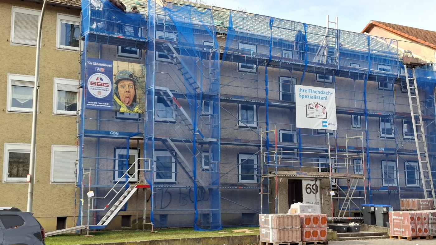 Dreigeschossiges Gebäude mit Gerüst und Netz, Gebäudevorderseite, Baumaterial auf dem Gehweg