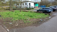 links verschmutzte Grünfäche mit Fahrzeugen im Hintergrund, rechts Zufahrt
