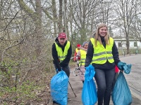 Vier Personen mit gelben Warnwesten tragen große, blaue Müllsäcke oder Unrat