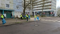 5 Personen mit Warnwesten heben mit Greifzangen achtlos weggeworfenen Müll auf der Straße und dem Gehweg auf.