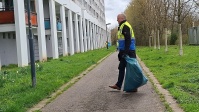 Mann mit Warnweste läuft mit vollem blauen Müllsack auf Grünstreifen zu.
