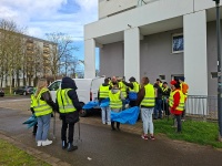 Mehrere Personen mit gelben Warnwesten, blauen Müllsäcken und Greifzangen auf einem Weg.