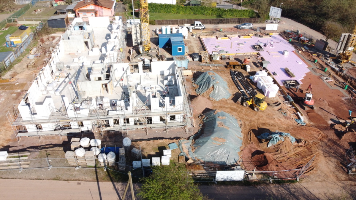 Drohnenaufnahme der Baustelle mit 1. Gebäude links mit Erdgeschoss und Mauern 1. Etage, hinten rechts Bodenplatte 2. Gebäude.