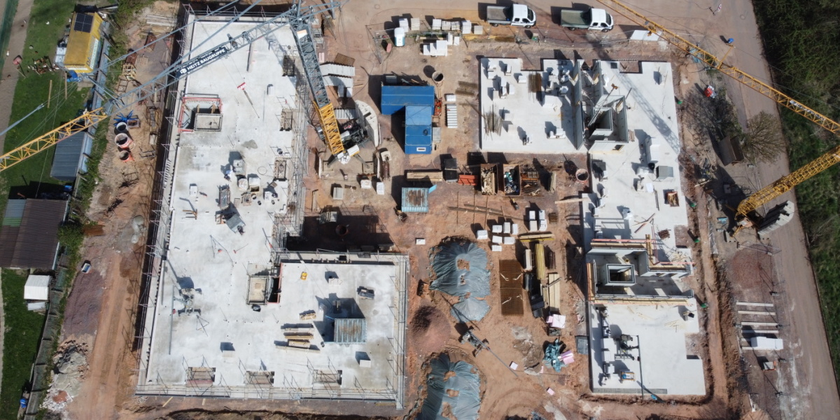 Luftbildaufnahme der Baustelle; linker Baukörper mit 2 Etagen und Gerüst, rechter Baukörper Bodenplatte und teilweise gemuert