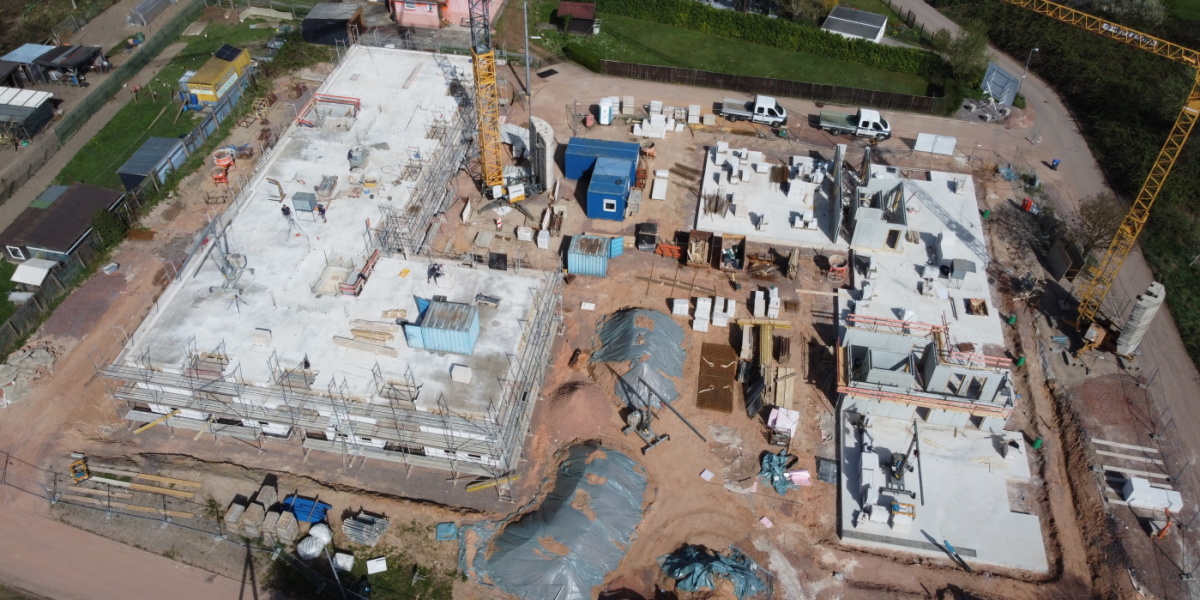 Luftbildaufnahme der Baustelle; linker Baukörper mit 2 Etagen und Gerüst, rechter Baukörper Bodenplatte und teilweise gemuert