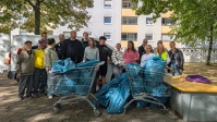 mehrere Personen zusammen mit gefüllten blauen Müllsäcken in Einkaufswagen, im Hintergrund Wohnhaus